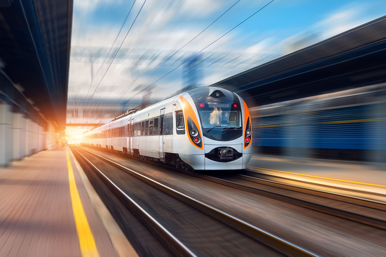 Beautiful train in motion at the railway station at sunset in Europe. Modern intercity train on the railway platform with motion blur effect. Industrial scene with moving passenger train on railroad